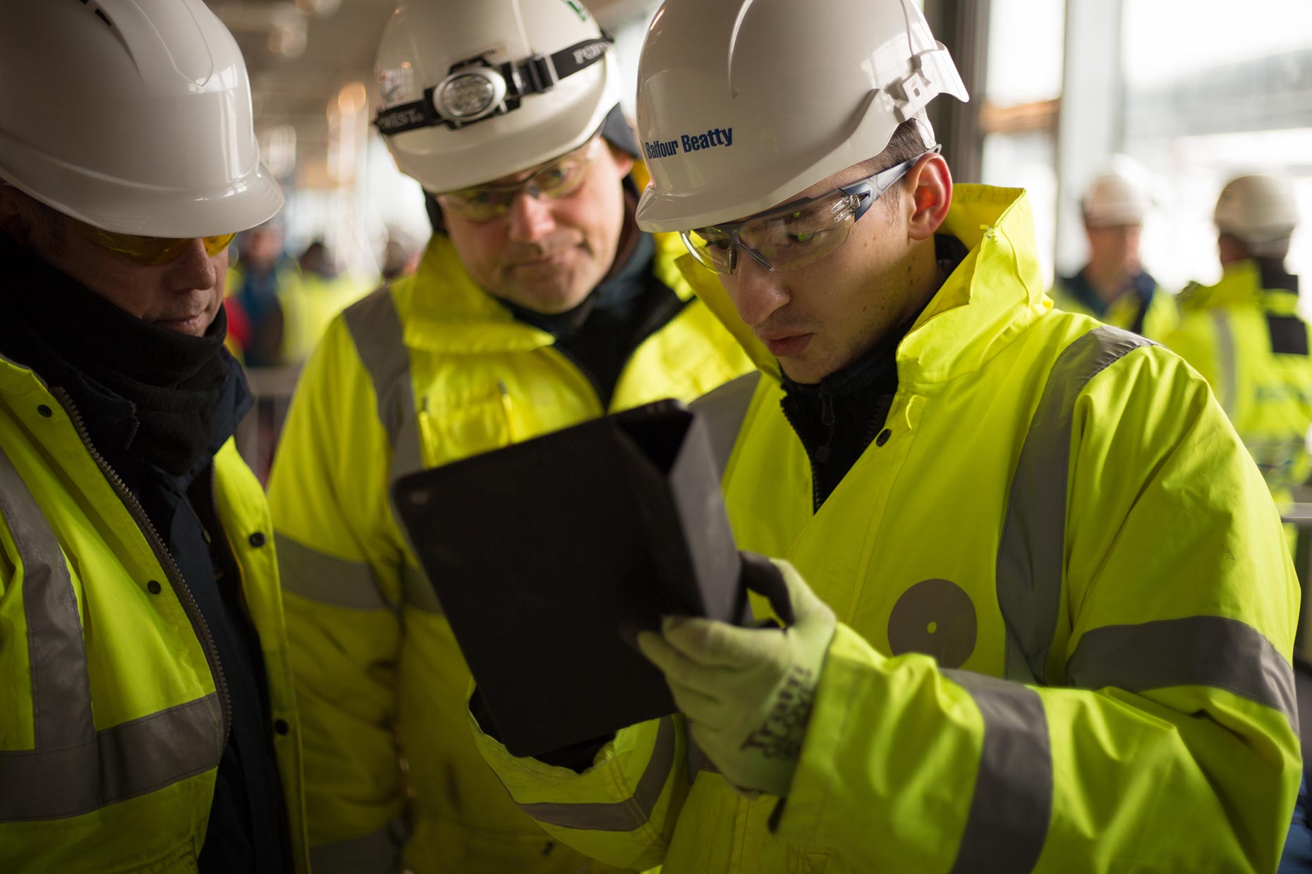 Corporate workers engineers in high-viz vests examine an ipad.